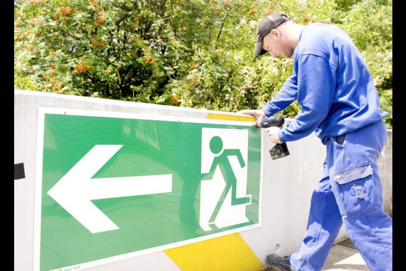 Mann montiert Fluchtwegeschild.