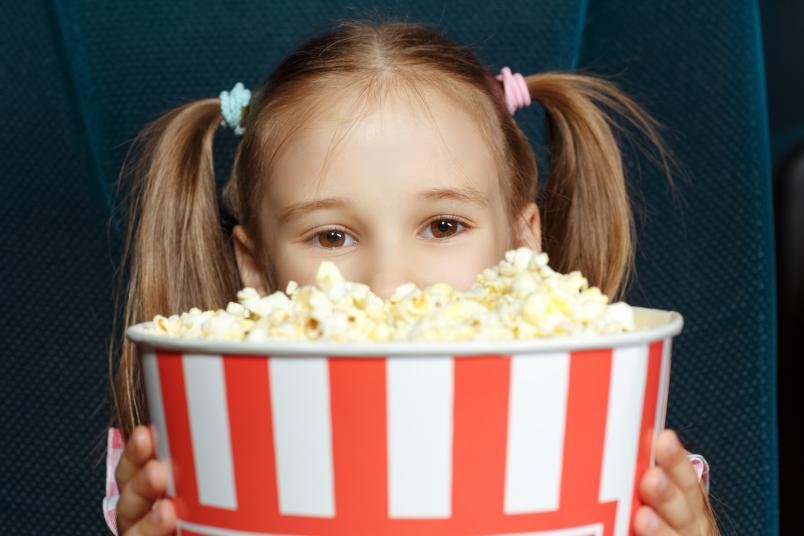 Mädchen schaut hinter einer Tüte Popcorn hervor.