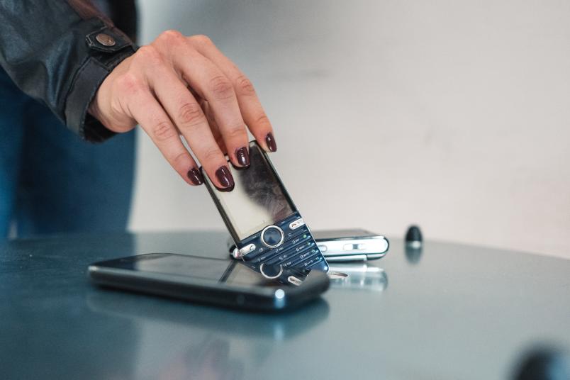 Eine Hand wirft ein altes Handy in einen Schlitz in einer Box.
