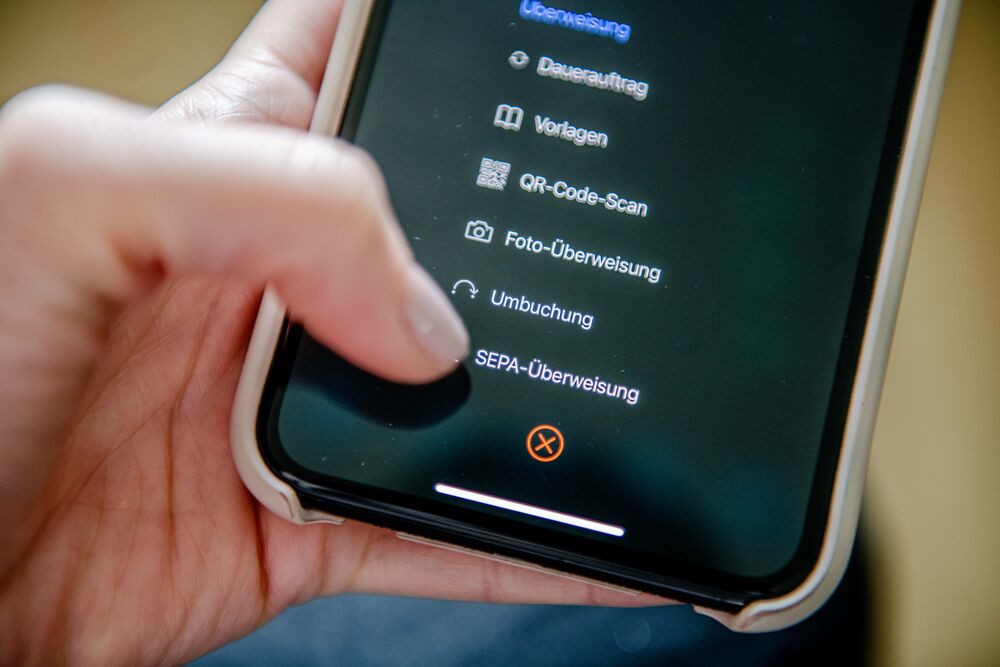 Eine Person tippt auf einem Smartphone auf den Menüpunkt "SEPA-Überweisung"