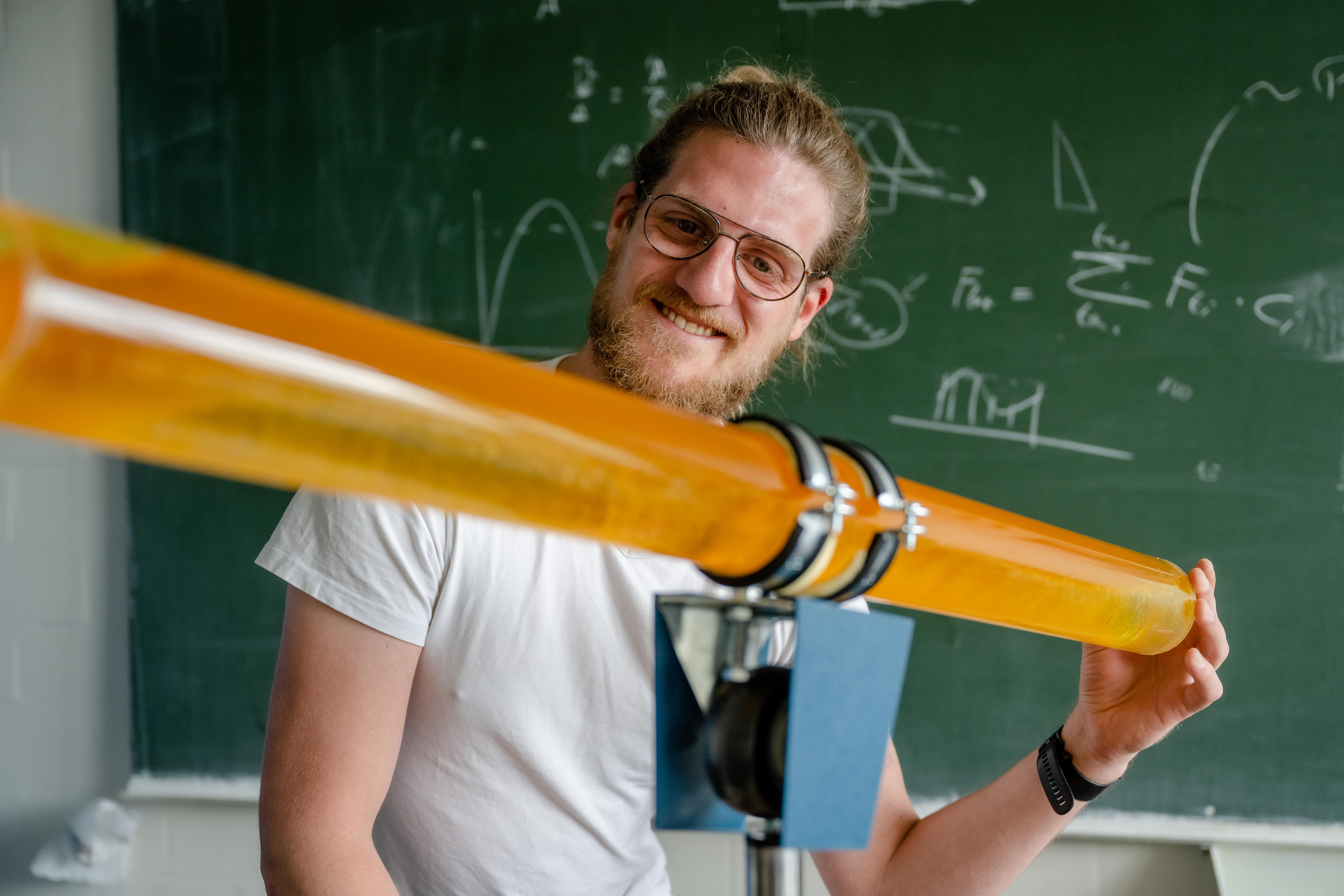 Eine Person sitzt hinter einer Plexiglasröhre mit einer orangenen Flüssigkeit.