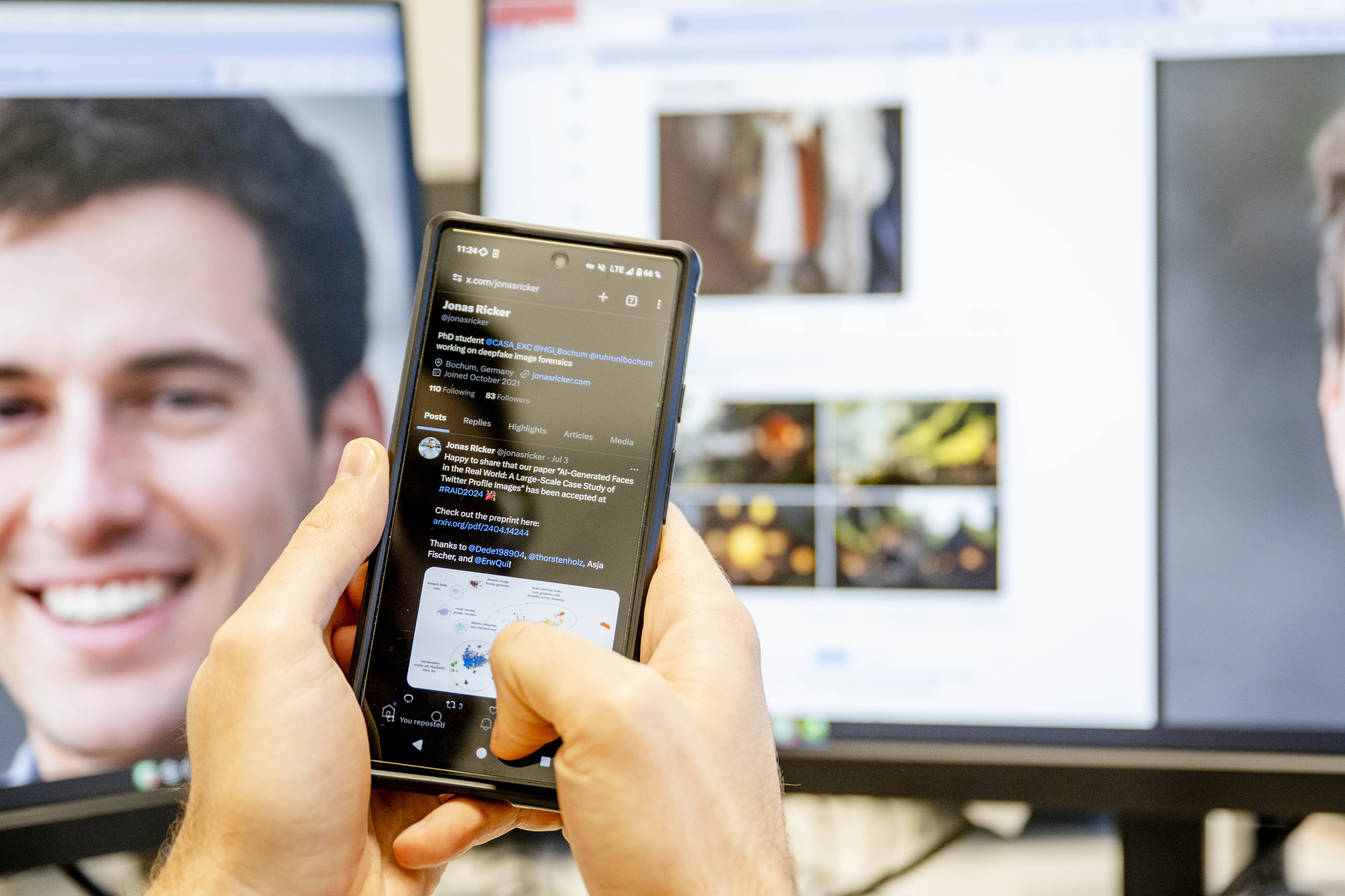 Twitter-Account auf Handy, im Hintergrund ein Monitor mit einem Personenfoto