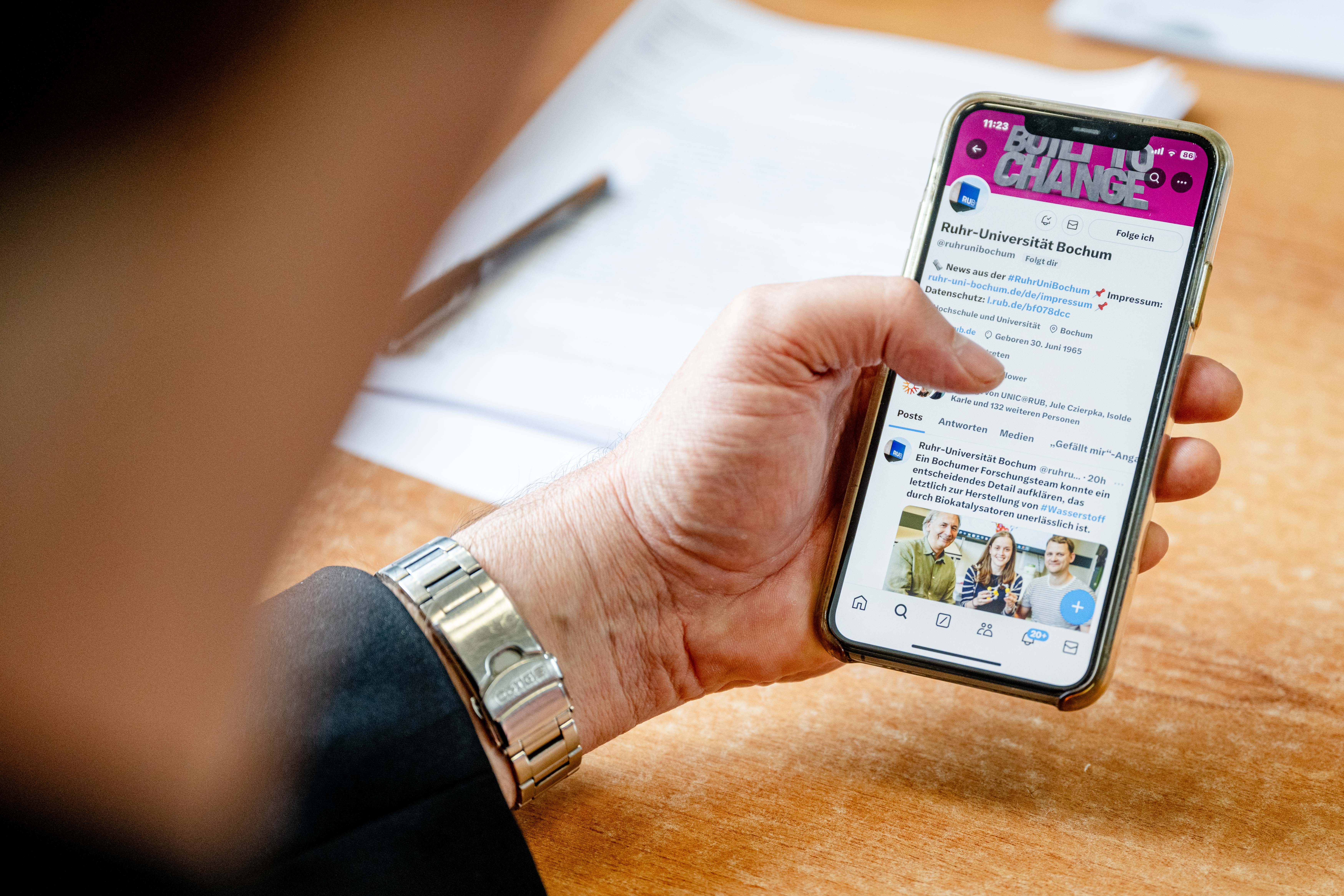 Eine Person hält ein Smartphone in der Hand auf dem der X-Account der Ruhr-Uni zu sehen ist.