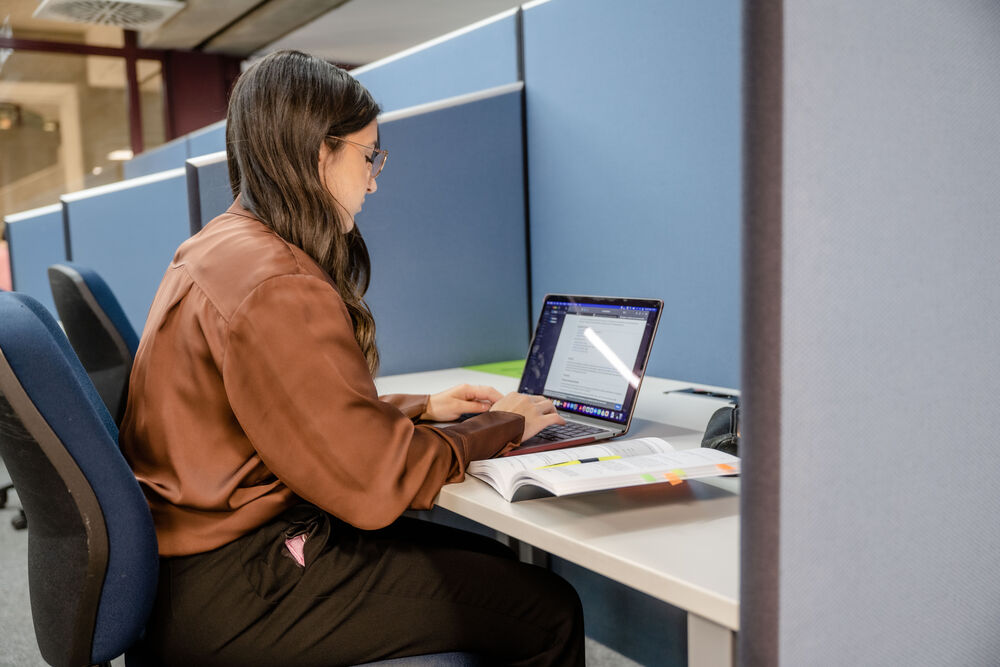 Studentin sitzt an einem Schreibtisch und schreibt auf dem Laptop. 