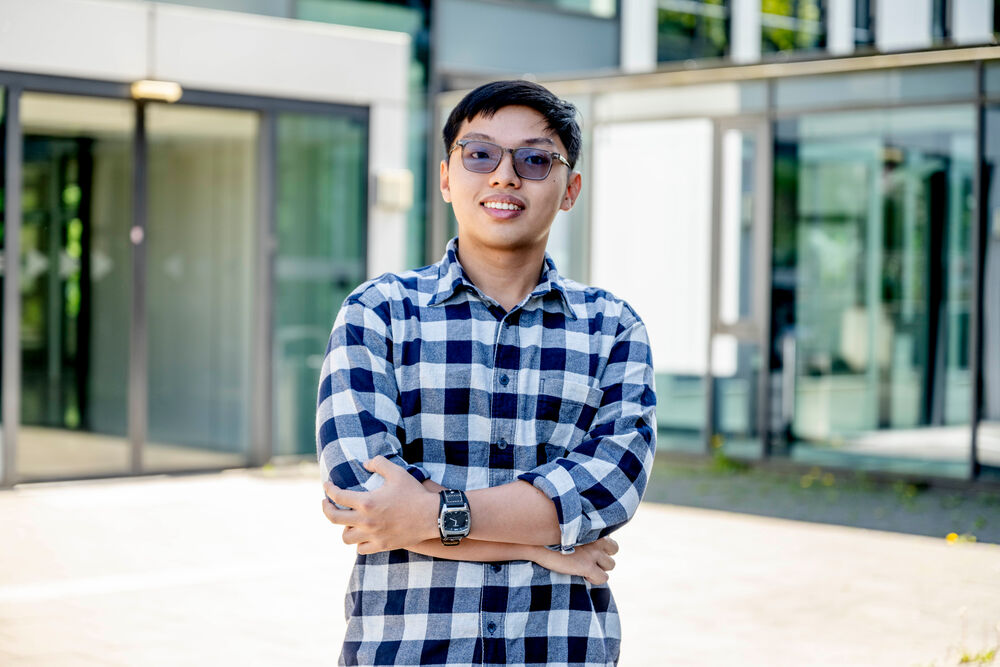Student mit Sonnenbrille steht vor einem Glaseingang. 