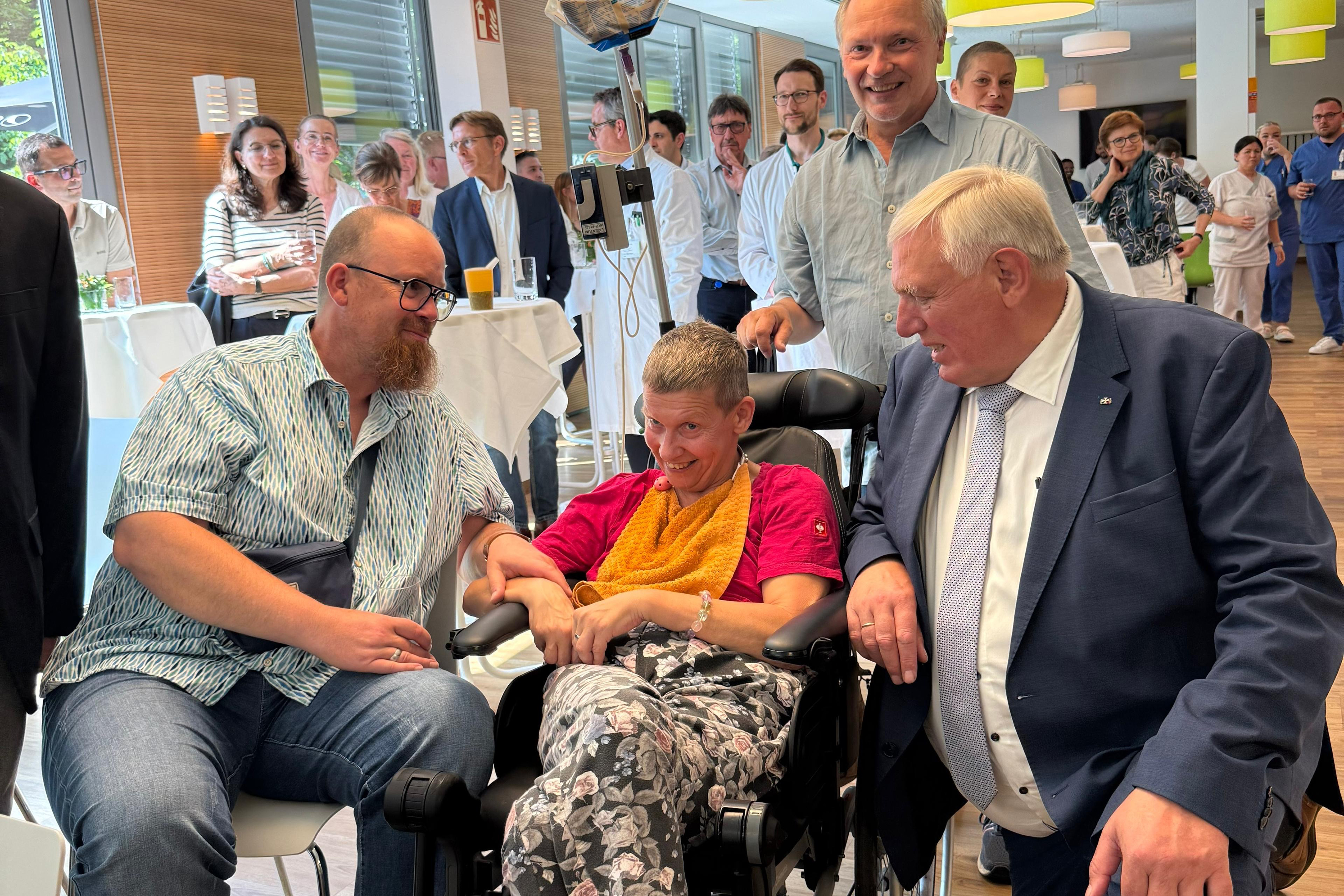 Minister Laumann kniet neben einer Patietin im Rollstuhl