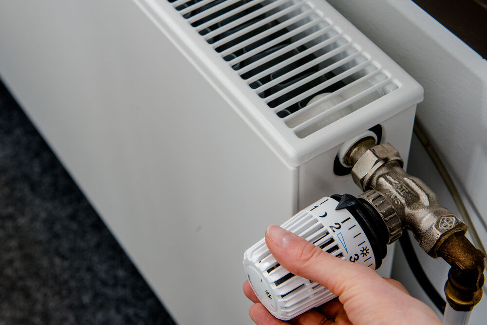 Eine Hand am Thermostat eines Heizkörpers