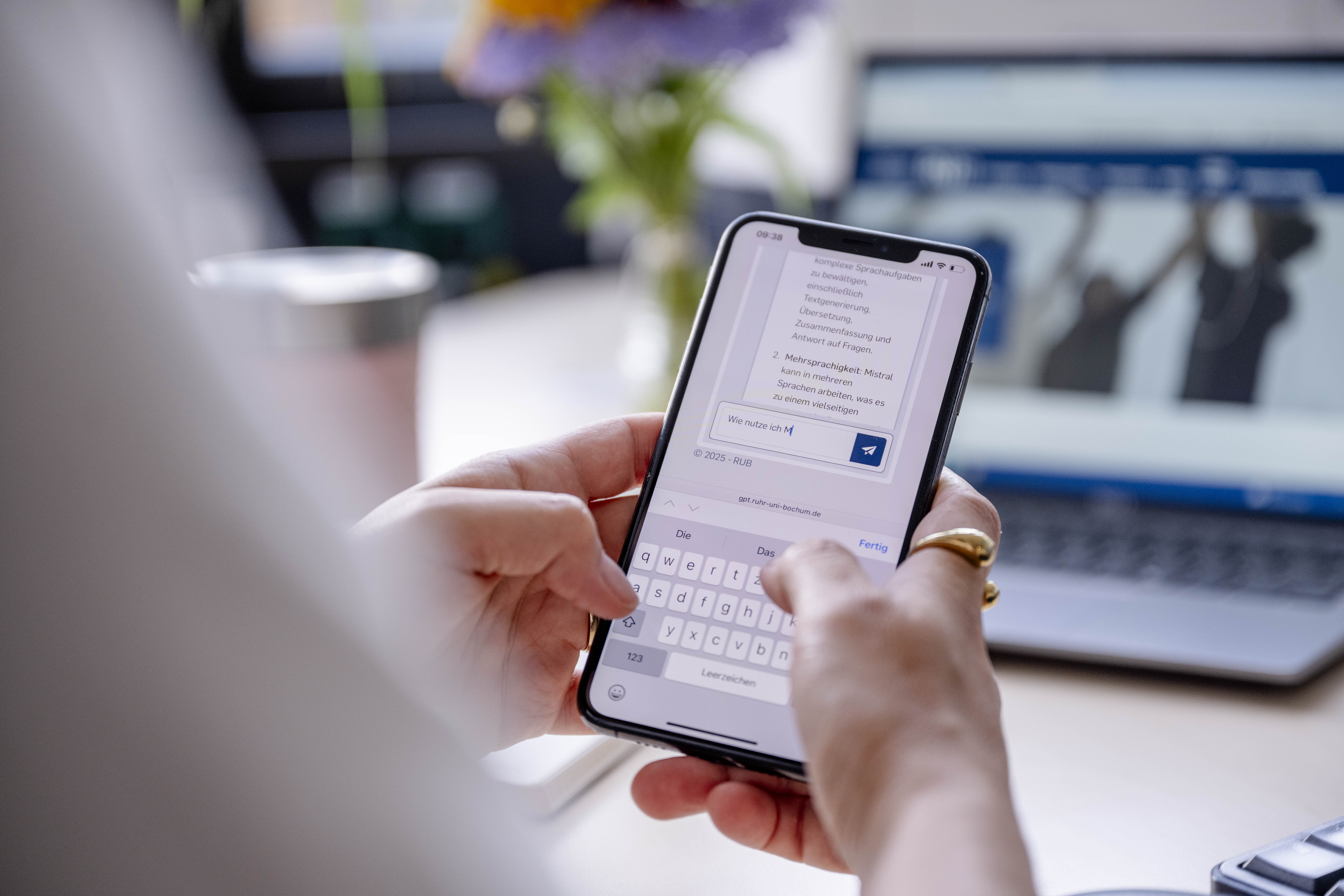 Blick über die Schulter einer Person. Sie hält ein Smartphone in der Hand. Darauf ist ein Chat mit dem LLM Mistral zu sehen.