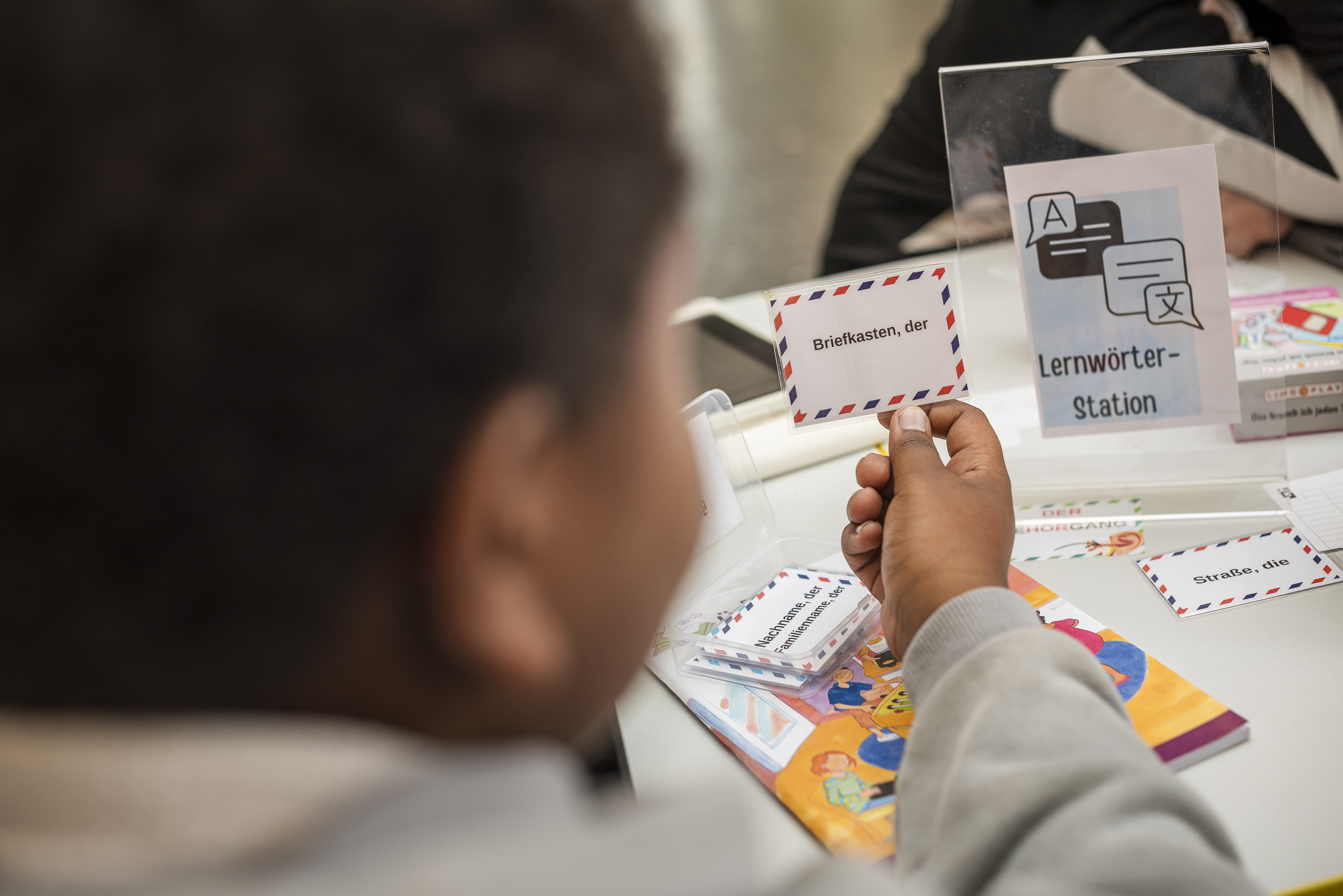 Ein Kind hält eine laminierte Karte mit der Aufschrift ""Briefkasten, der"
