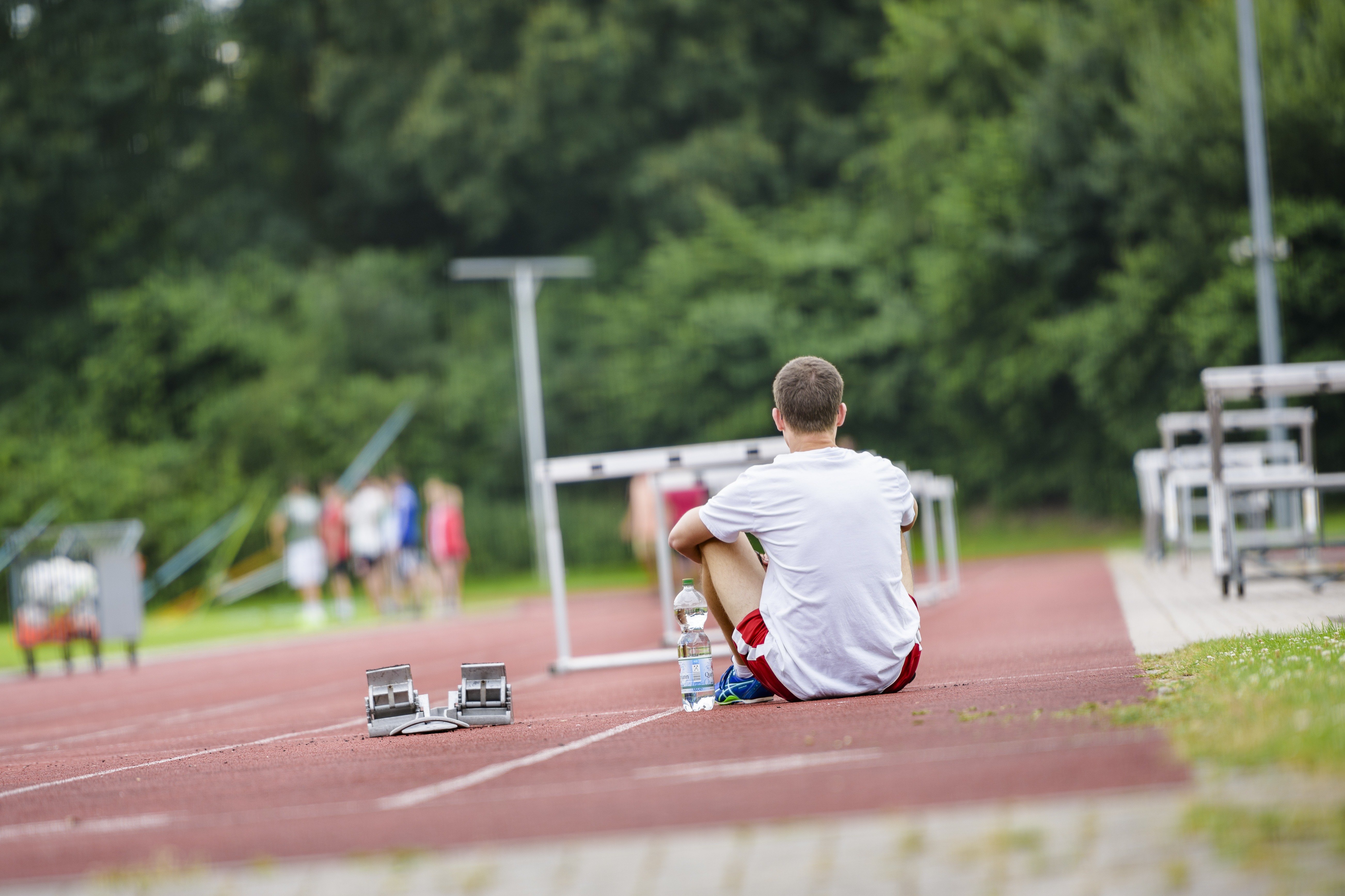 Sportler sitzt auf einer Tartanbahn.