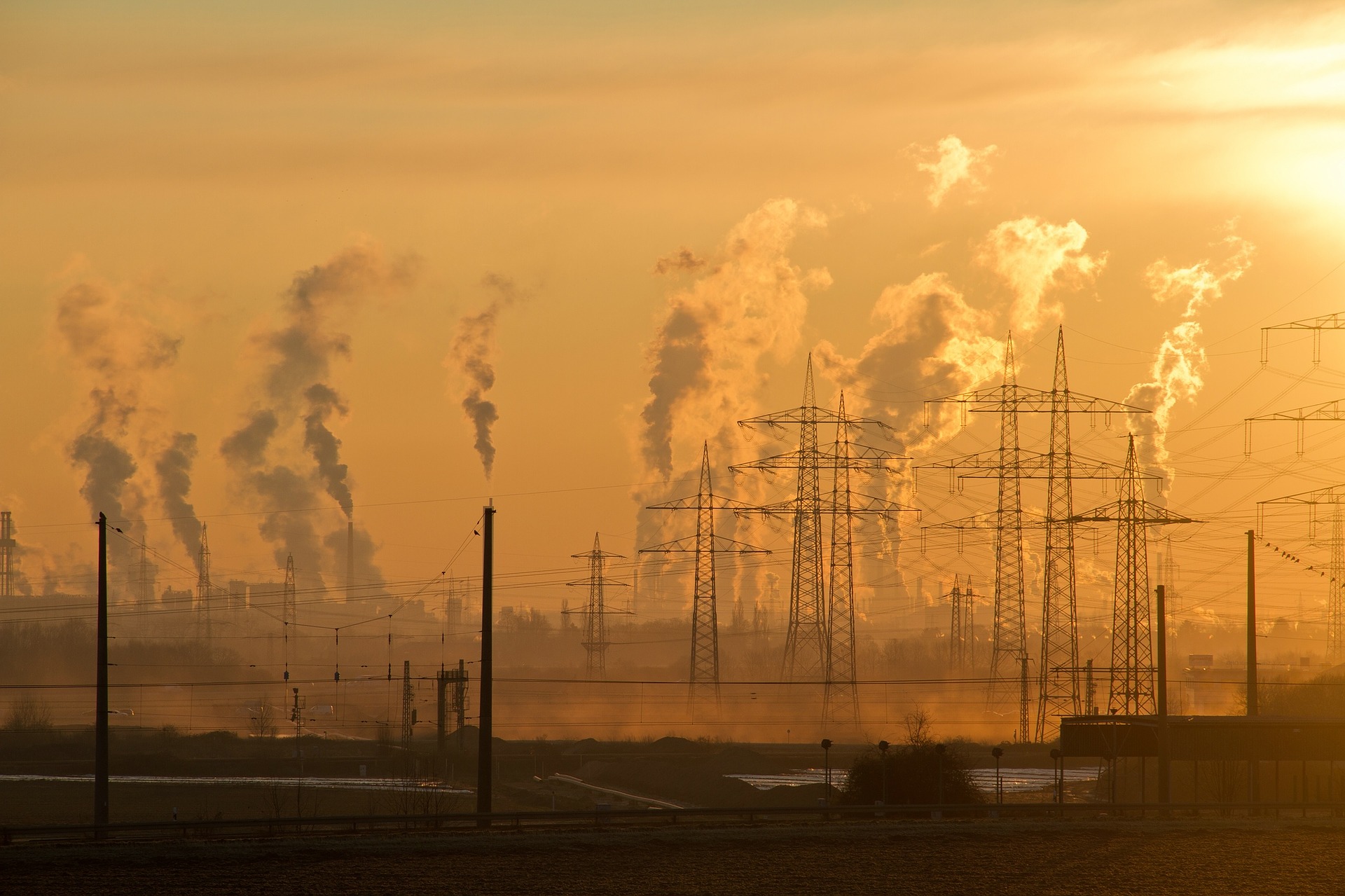 Stromleitungen und rauchende Industrieschornsteine im Sonnenuntergang