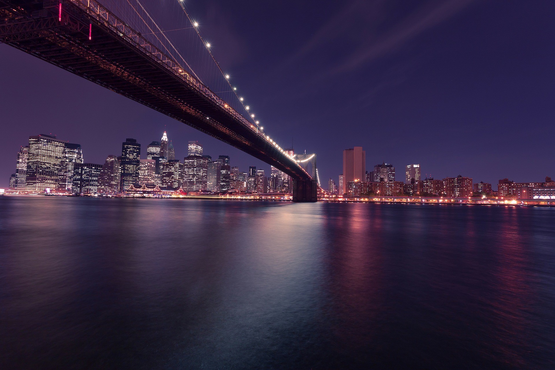 Skyline von New York City bei Nacht – im Vordergrund die markante Brooklyn Bridge