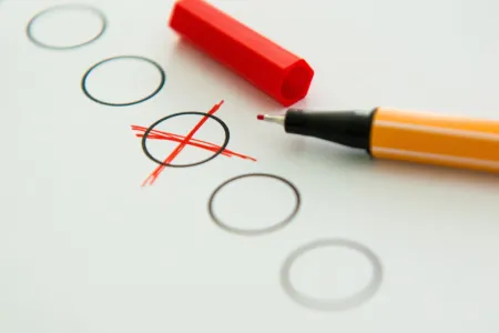 Mehrere schwarze Kreise auf einem Blatt Papier. Ein Kreis ist mit einem roten Kreuz durchgestrichen. Es liegt ein roter Stift daneben. 