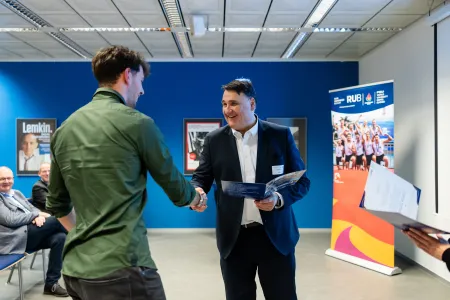 Rektor Martin Paul zeichnet einen Studierenden mit einer Urkunde aus.