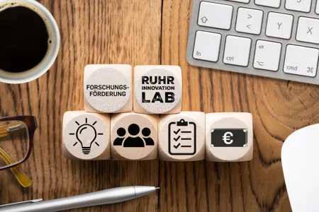 Mehrere Holzwürfel mit Symbolen wie einer Glühbirne, einer Menschengruppe und dem Logo des Ruhr Innovation Lab