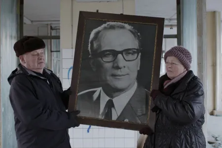 Eine Frau und ein Mann halten ein großes Foto von Erich Honecker
