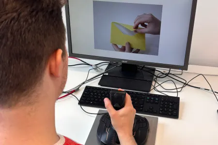 Blick über die Schulter eines Mannes, der mit Joystick am Computerbildschirm sitzt