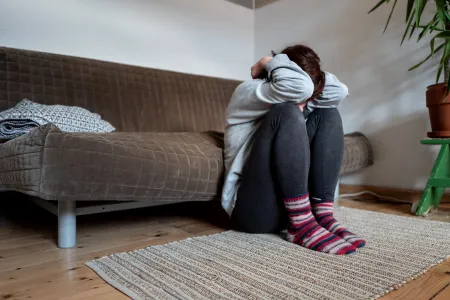 Eine Frau, die den Kopf zwischen den Armen hat und vor einem Sofa hockt