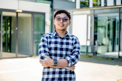 Student mit Sonnenbrille steht vor einem Glaseingang. 