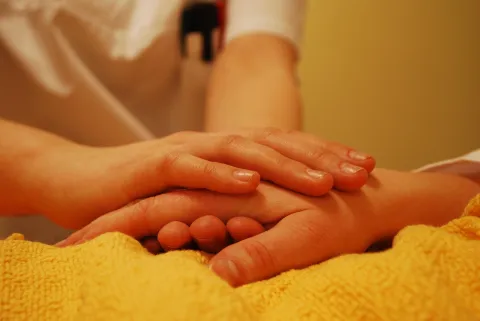 Eine Frau hält die auf einer Decke liegende Hand einer Person. 