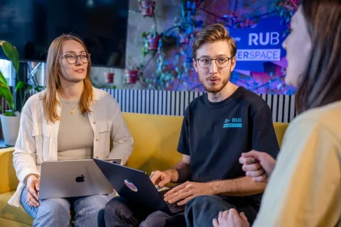Zwei Frauen und ein Mann unterhalten sich und sitzen auf einem Sofa. 
