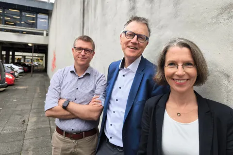 Zwei Männer und eine Frau lehnen an einer Wand