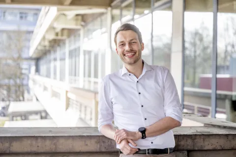 Mann im weißen Hemd lehnt an einer Brüstung und lacht