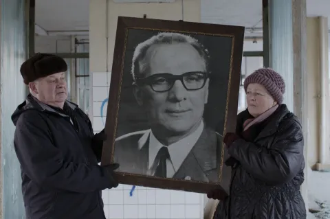 Eine Frau und ein Mann halten ein großes Foto von Erich Honecker