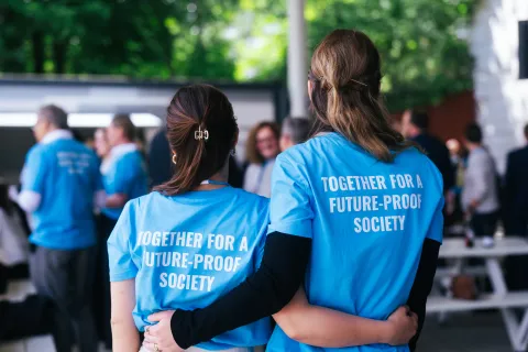 Zwei Personen von hinten, Arm im Arm, in blauen T-Shirts mit der Aufschrift "Together for a future-proof society"