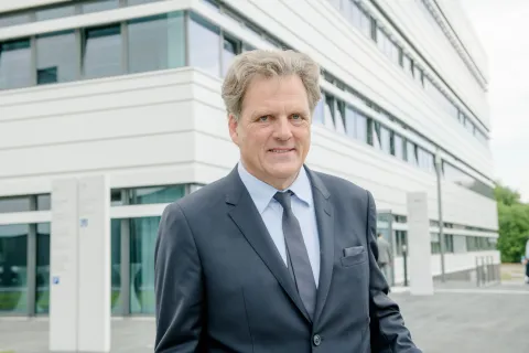 Porträt eines Mannes im grauen Anzug vor einem weißen Gebäude