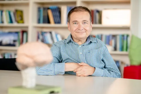 Ein Mann im karierten Hemd lächelt in die Kamera, vor ihm steht ein Gehirnmodell