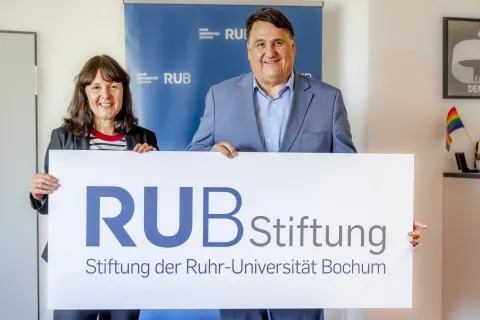 Porträt von Susanne Seiler und Martin Paul mit einem Schild mit der Aufschrift "RUB Stiftung"