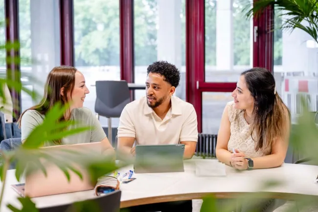 3 Studierende sitzen vor einem Laptop.