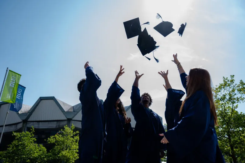 Studierende werfen Doktorhüte in die Luft. 