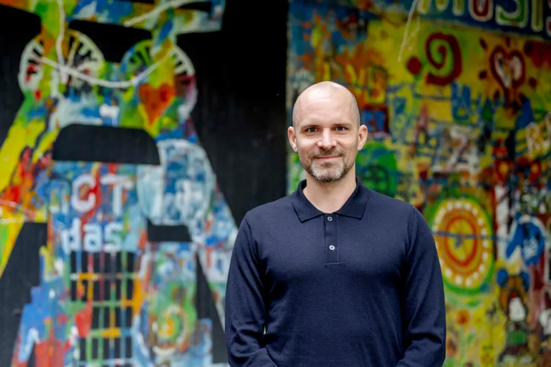 Ein Mann in einem blauen Pullover vor einer bunt bemalten Wand