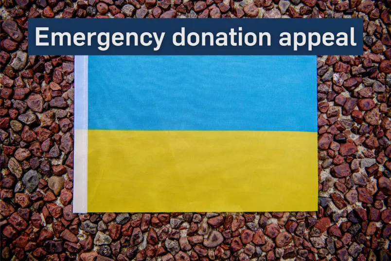 Ukranian flag resting on a stone surface with the message 'Emergency donation appeal' placed over the image.