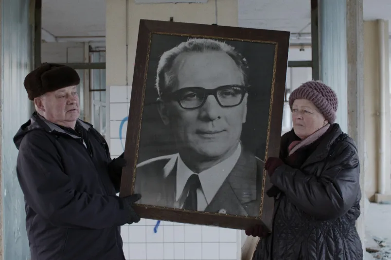 Eine Frau und ein Mann halten ein großes Foto von Erich Honecker