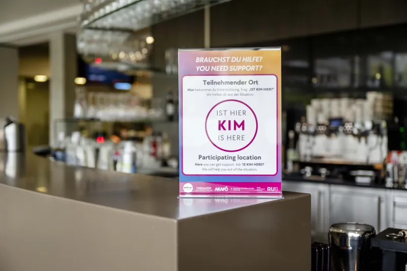 Theke in einer Cafete, darauf ein Schild, das ausweist, dass dieser Ort an der Kampagene "Kim ist hier" teilnimmt.
