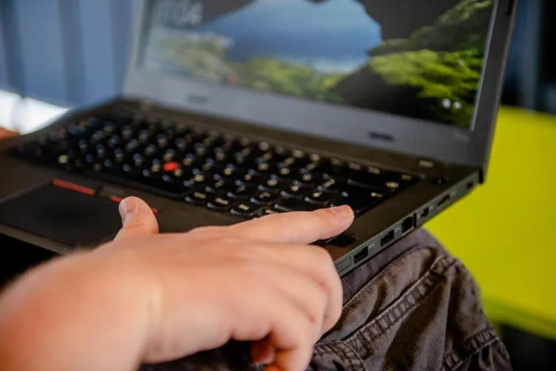 Ein aufgeklapptes Notebook auf den Knien einer Person