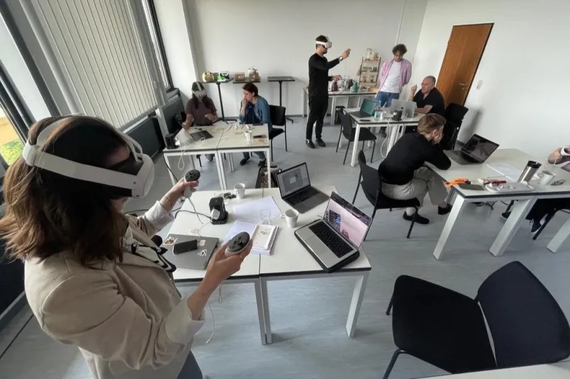 Eine Frau mit VR-Brille in einem Seminarraum mit weiteren Menschen