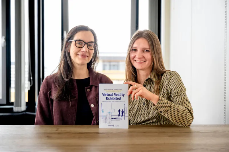 Zwei Frauen halten ein Buch in die Kamera