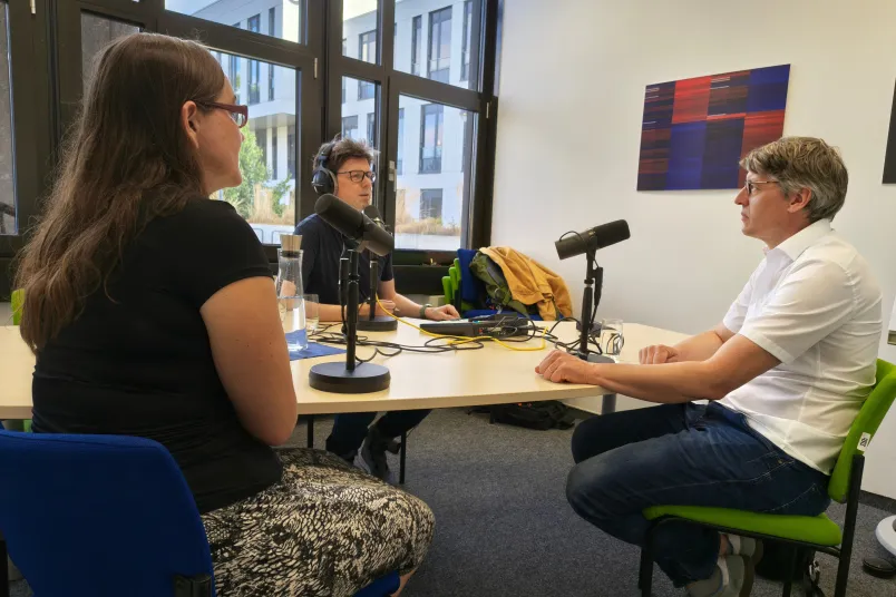 Drei Personen am Tisch vor Mikrofonen