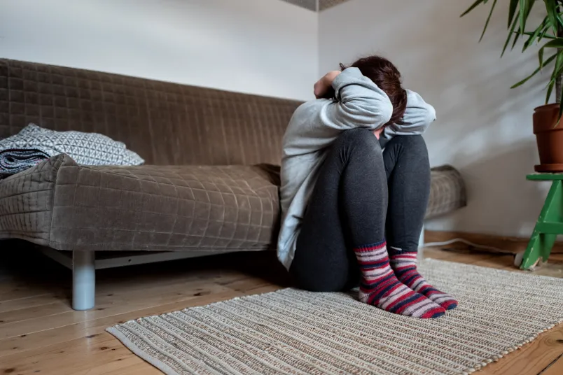 Eine Frau, die den Kopf zwischen den Armen hat und vor einem Sofa hockt