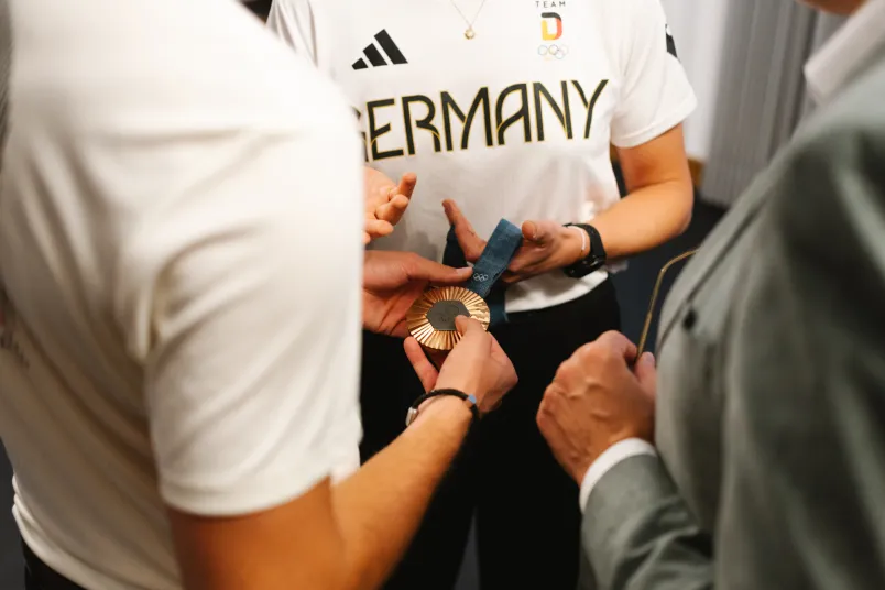 Männer und Frauenhände halten eine olympische Medaille