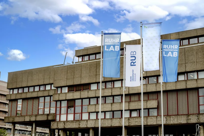 Flaggen der RUB, der TU Dortmund und des Ruhr Innovation Lab vor der Universitätsbibliothek