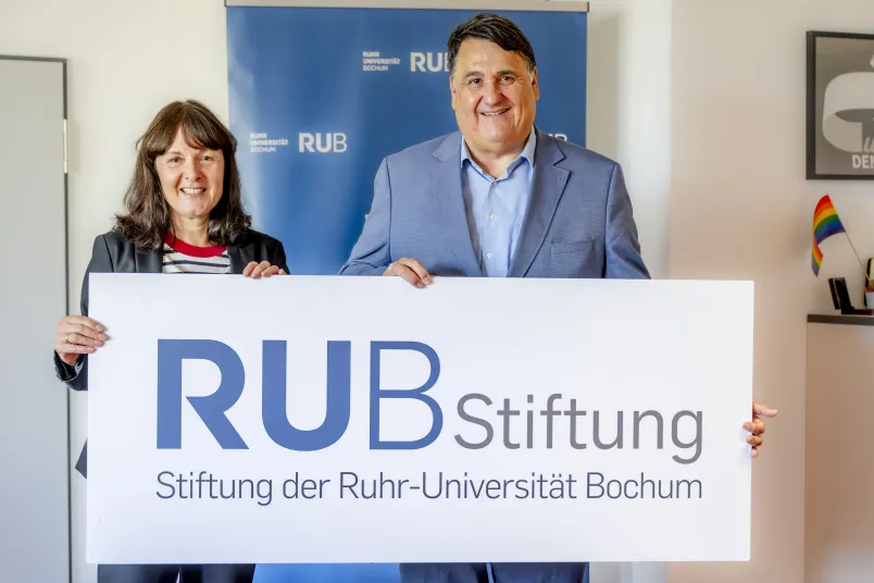 Porträt von Susanne Seiler und Martin Paul mit einem Schild mit der Aufschrift "RUB Stiftung"