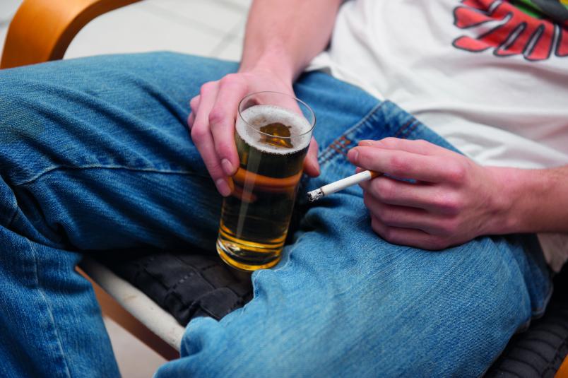 Ein Mann mit einer Zigarette  und einem Glas Bier in der Hand.