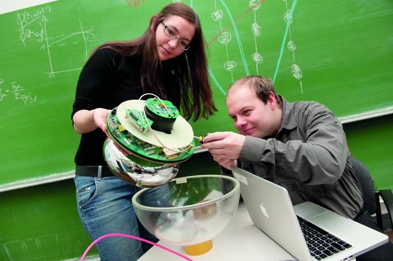 Ein Mann und eine Frau setzen eine elektronische Apparatur in eine Glaskugel.