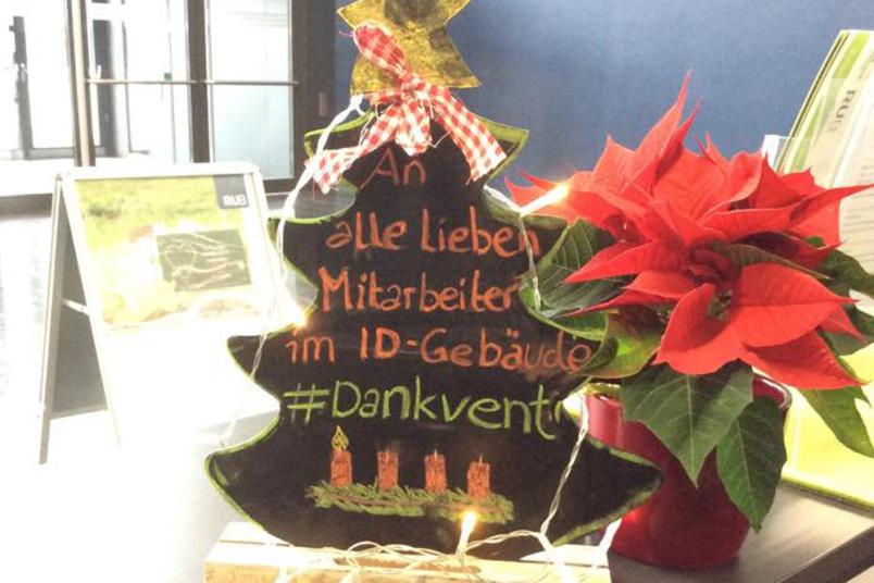Eine bunt geschmückter, kleiner Tannenbaum aus Holz mir der Beschriftung "An alle lieben Mitarbeiter im ID-Gebäude. #Dankvent"