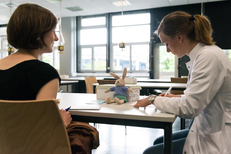 Plüschhase sitzt vor Ärztin auf einem Tisch.